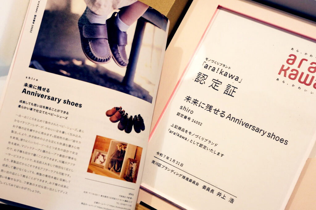 東京・荒川区のブランド「ara!kawa」認定証。初心者向けのベビーシューズが、高い技術力を認められた証です。紫色の柔らかな革靴の写真と共に、地域の誇りとして「未来に残せるAnniversary shoes」が認定された書面です。
